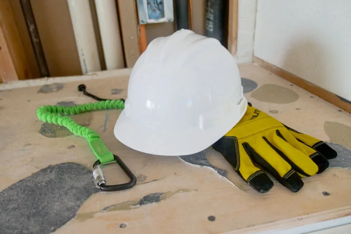 White hard hat, yellow gloves and a safety lanyard on a workbench