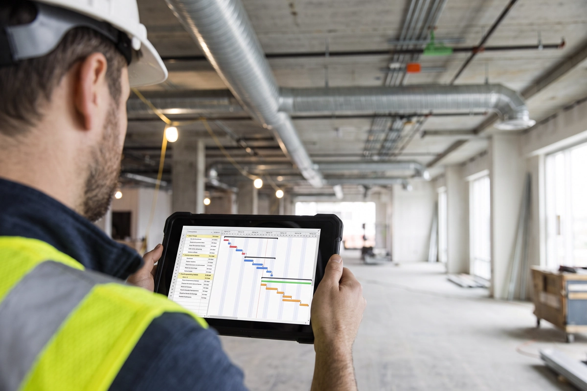 Construction professional reviewing a project programme on a tablet beneath ductwork